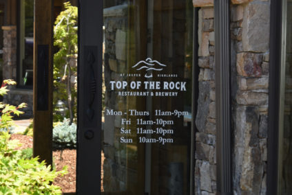 Top of the Rock restaurant and brewery vinyl sign on an open door showing their hours