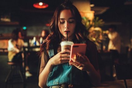 Young woman in a dark room with coffee in hand looking at her smart phone